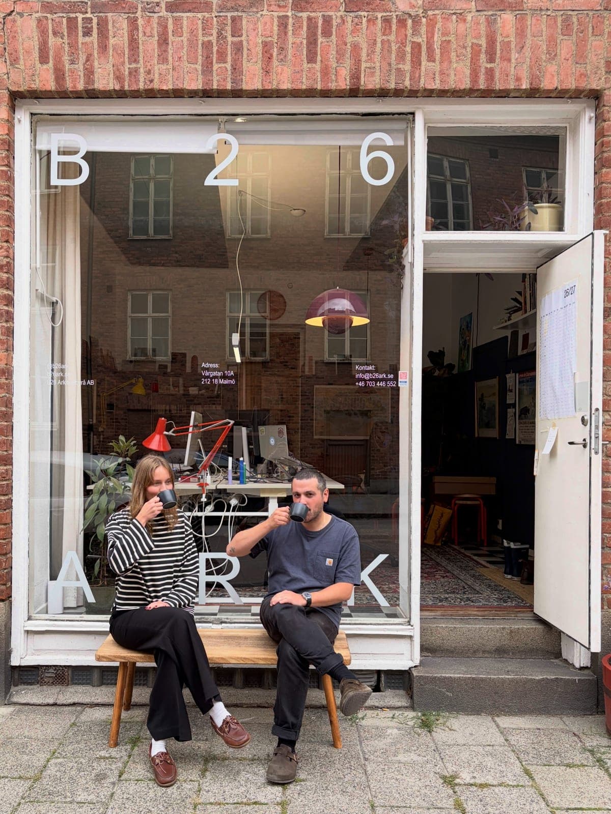 Två arkitekter dricker kaffe på en bänk framför B26:s skyltfönster på Vårgatan i Malmö